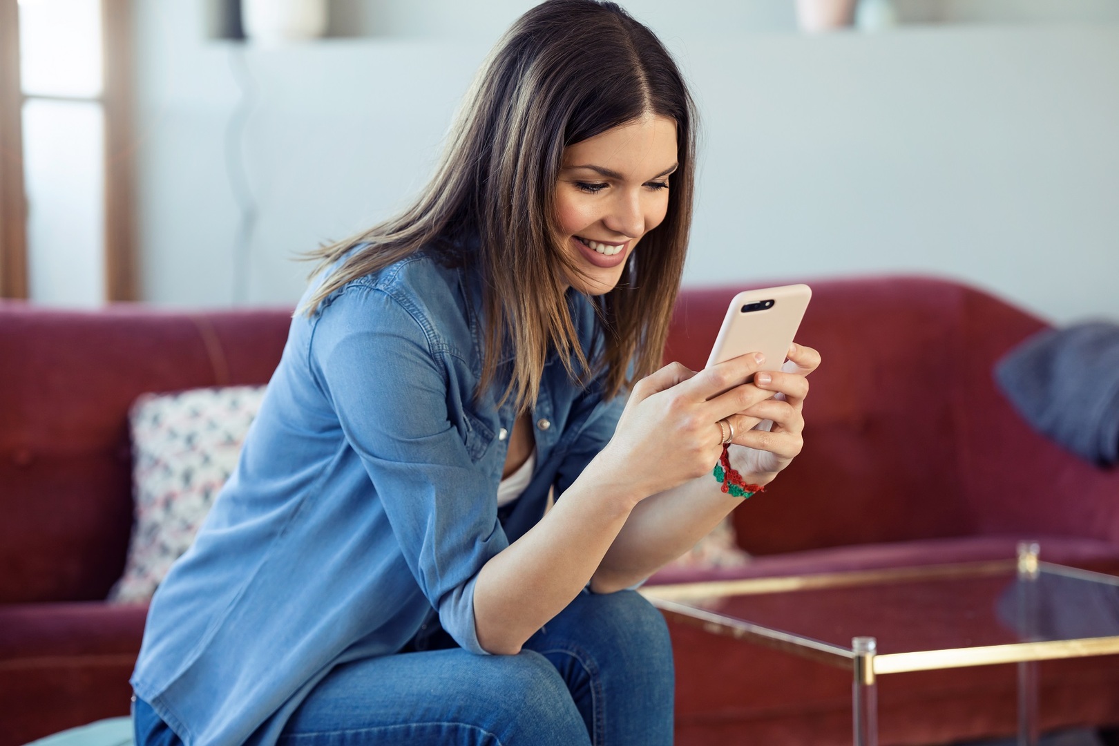 Pretty young woman using her mobile phone while sitting on sofa